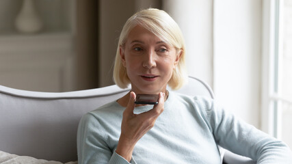 Elderly woman holding smartphone uses virtual voice assistant