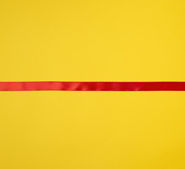 Obraz premium red silk ribbon on a yellow background, festive backdrop
