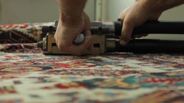 A man cuts a carpet with a special loom. We see only his hands, a close-up of the machine. Beautiful oriental carpet in preparation.