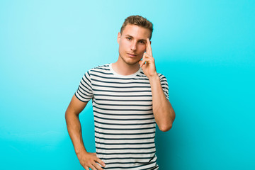 Young caucasian man against a blue wall pointing temple with finger, thinking, focused on a task.