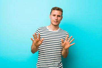 Young caucasian man against a blue wall rejecting someone showing a gesture of disgust.