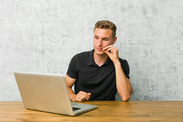 Young entrepreneur working with his laptop on a desk with fingers on lips keeping a secret.