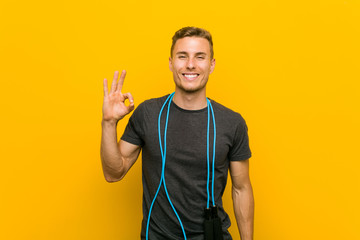 Young caucasian man holding a jump rope cheerful and confident showing ok gesture.