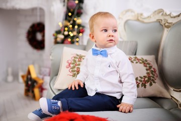 baby boy in a bright shirt and tie sitting on the sofa on the background of Christmas decor.