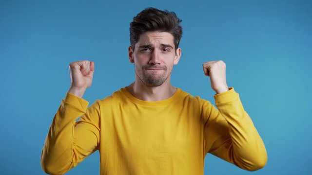Yes winner gesture. Happy european man dancing. Handsome guy with stylish hairdo surprised to camera over blue background. 4k