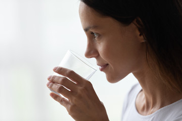 Closeup face of beautiful 30s woman holds glass of water