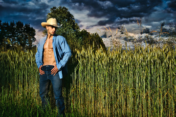 Portrait of sexy farmer or cowboy in hat with unbuttoned shirt on muscular torso, looking to a...