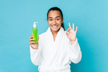 Young mixed race indian holding an aloe vera bottle cheerful and confident showing ok gesture.