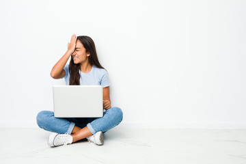 Young mixed race indian woman sitting working on laptop forgetting something, slapping forehead...