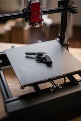 Black revolver gun lying on working surface of modern 3d printer