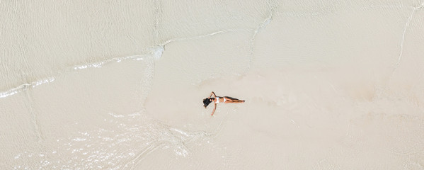 Aerial drone shot of woman lying in water on white sand beach and enjoying vacations. Tropical travel concept.