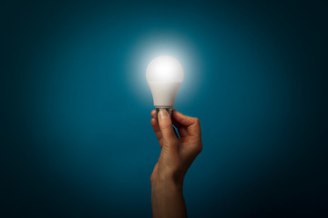 Female hand holds a working LED lamp on a blue background. Energy saving concept, alternative...