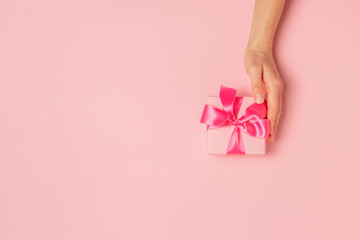 Female hands hold, take, receive a gift on a pink background. Wedding concept, Valentine's Day, a gift for a loved one. Flat lay, top view