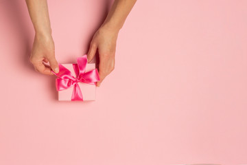 Female hands hold, take, receive a gift on a pink background. Wedding concept, Valentine's Day, a gift for a loved one. Flat lay, top view