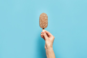 Female hand holds ice cream on a stick on a blue background. Concept of hot summer, stress. Flat...