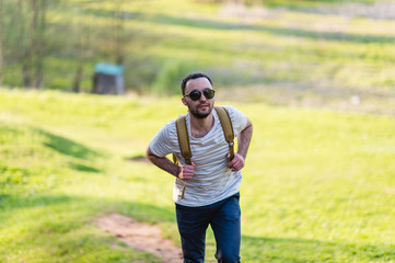 Hiking man portrait with backpack walking in nature. Caucasian man smiling happy with forest in background during summer trip
