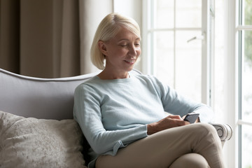 60s blonde woman using smart phone chatting online with friend