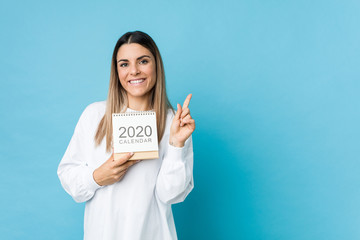 Young caucasian woman holding a 2020 calendar smiling cheerfully pointing with forefinger away.