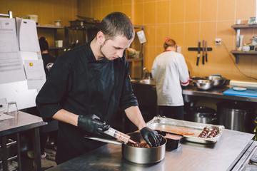 Theme cooking. A young Caucasian man in black uniform and latex gloves at a restaurant in the kitchen. Cooking mincers into a berry with a syringe. A dish of figs, fig fruit fig tree or Ficus Carian