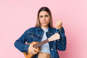 Fototapeta premium Young caucasian woman playing ukelele showing fist to camera, aggressive facial expression.