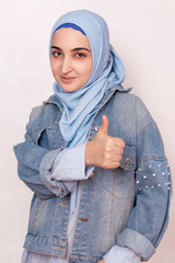 Fashion portrait of stylish Muslim girl in jean jacket giving thumbs up. Modern and young middle-eastern girl in hijab with denim jacket and doing happy thumbs up gesture. Recommending service