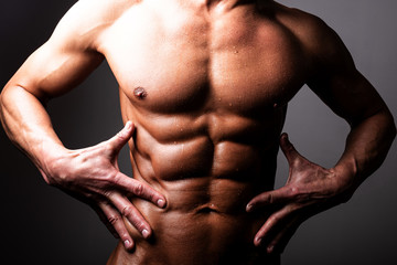 Beautiful, athletic, male torso. In contrast lighting. A man holds his hands near the press.