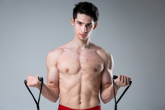Studio portrait young Caucasian man on gray background posing. theme of puberty, problem skin, teen acne. Caucasian athlete uses banding for fitness. Allergy sports nutrition, supplements steroids