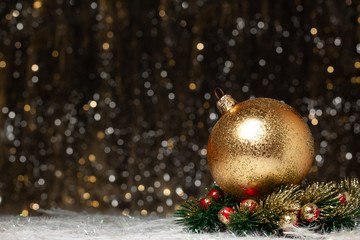 Christmas decorations view of  gold evening ball with gold glitter on it in christmas wreath with red berries of the right site on dark background with silver and gold colors bokeh. Copy space