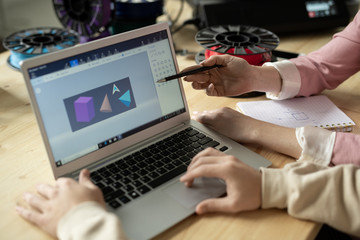 Hands of creative designers by laptop display with sketch of geometric figures