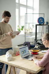 Young designer with tablet scrolling through online stuff by workplace