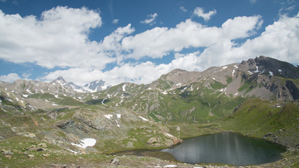 Circular mountain lake, called Tormotta Lake, with mountain peaks and cloudy sky in the background, italian alps