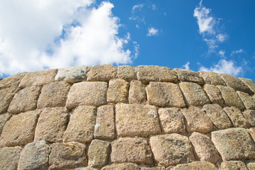 Close up of an Incan wall, made of squared stones smoothed and wedged one to each other. Blue sky and clouds in the background