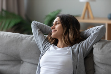 Woman put hands behind head leaned on couch resting indoors