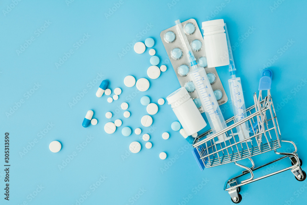 Wall mural pills and medical injection in shopping trolley on blue background. creative idea for health care co