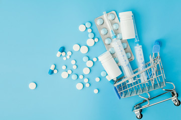 Pills and medical injection in shopping trolley on blue background. Creative idea for health care...