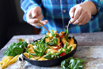 Selective focus. Chef hands mix pasta with vegetables and basil. Cooking vegan paste. Italian Cuisine.