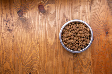 Dog food in bowl on wooden table. From above. Place for text