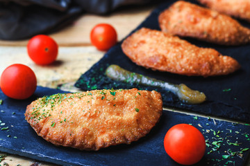 Portion and three small pasty homemade with tomatoes and applesauce on slate plate. Front view, no people. Food concept