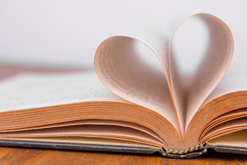 Old book and heart-shaped pages. White background. Wooden Table. Closeup