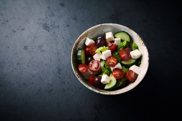 Salad with Kalamata Olives, Cucumber Cherry Tomatoes and Feta Cheese on black Stone Background. Healthy Snack Idea. Close up.
