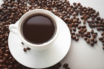 Cup of hot coffee with beans on light background