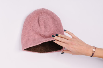 Hand of caucasian woman hold bilateral pink-brown knitted beanie hat. Warm winter wool self-made...