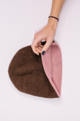 Hand of caucasian woman hold bilateral pink-brown knitted beanie hat. Warm winter wool self-made...