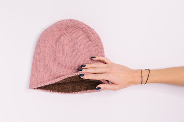 Hand of caucasian woman hold bilateral pink-brown knitted beanie hat. Warm winter wool self-made clothes. Flat lay, copy space. Knitting and crocheting concept. Alpaca wool. Copy space.