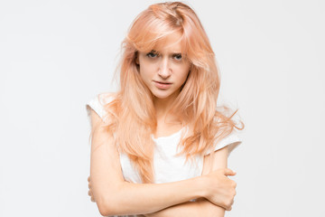 Close up studio portrait of young negative-minded blonde girl in white t-shirt. Woman crossed her arms over her chest and crossly look at camera. Angry and irritated female. Emotions concept.