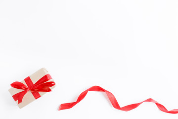 Scarlet ribbon and gift box in craft wrapping paper with red bow. White background, flat lay. Merry Christmas and Happy New Year concept. Nativity mood. Festive days. Copy space.
