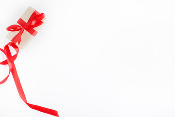 Scarlet ribbon and gift box in craft wrapping paper with red bow. White background, flat lay. Merry Christmas and Happy New Year concept. Nativity mood. Festive days. Copy space.