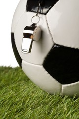 Single black and white soccer sports ball with referee whistle close up with selective focus on...