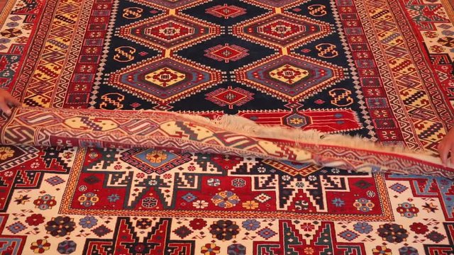 Large oriental rug with colorful patterns. Handmade rug production, carpet close-up with all the details. Hands unroll carpet rolled