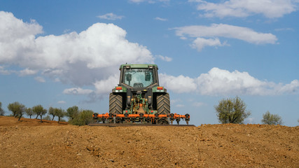 Obraz premium Tractor verde labrando un campo de almendros con nubes